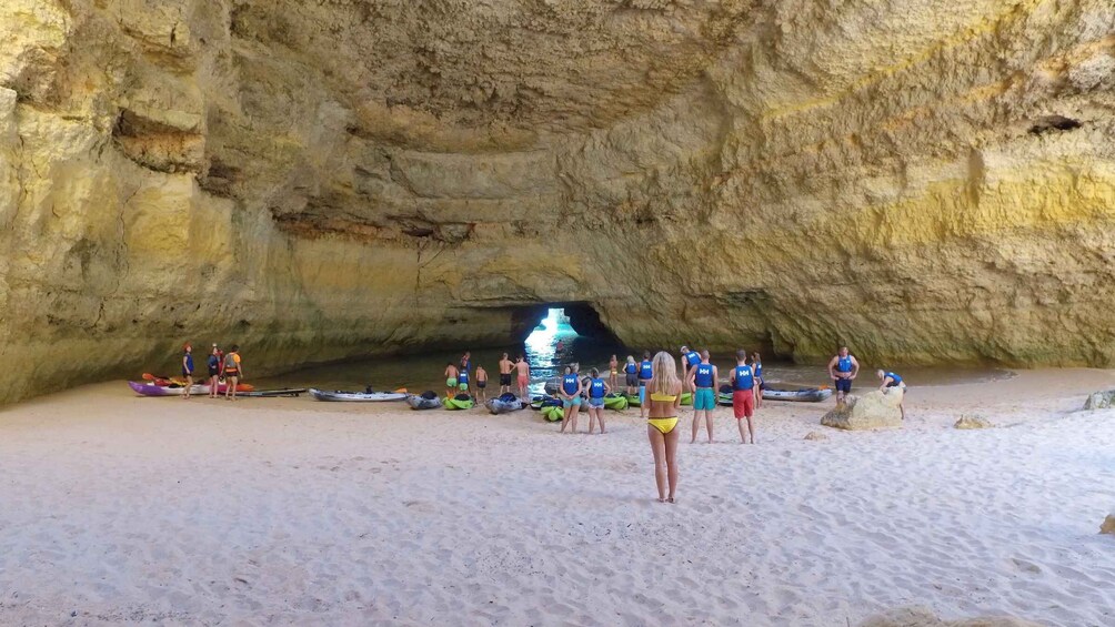 A group of people on a beach with kayaks and a cave entrance. 4