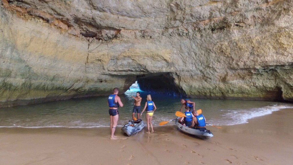 A group of people in kayaks on a beach with a cave in the background. 3