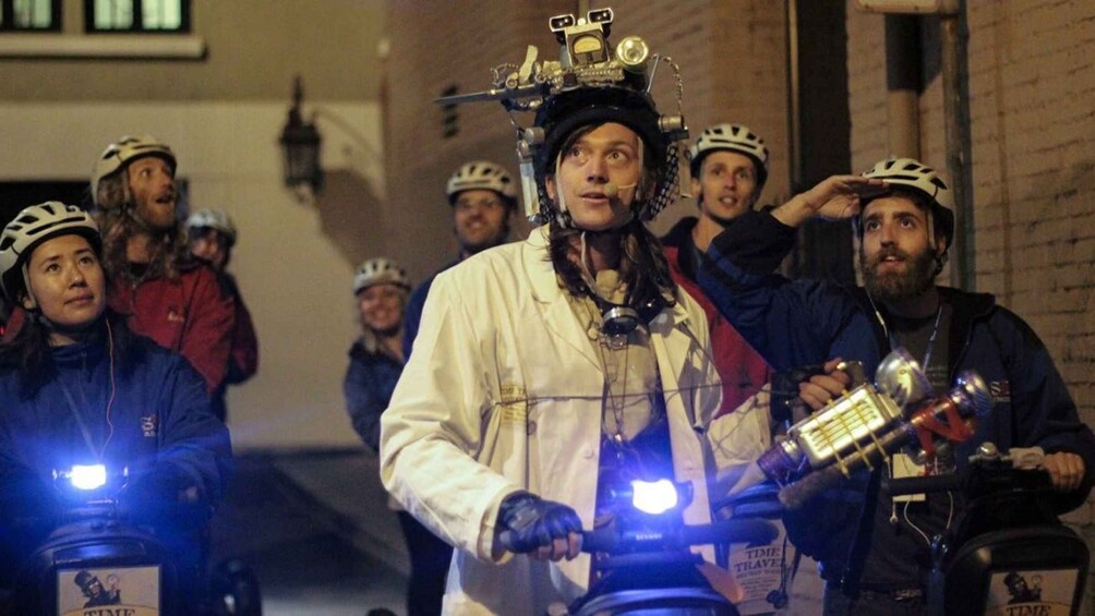 Una persona in bicicletta con casco e luci, circondata da altre persone con caschi e biciclette. 3