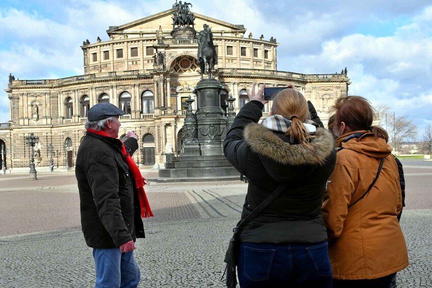 A group of people taking a photo in front of a large, ornate building with a statue in the center. 1