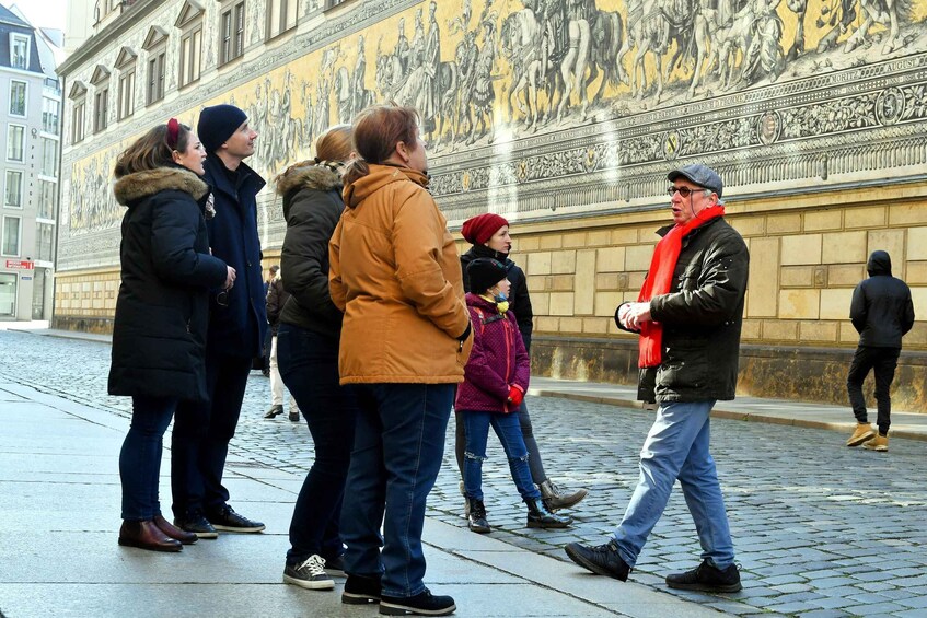 People standing and walking on a cobblestone street in front of a large mural. 4