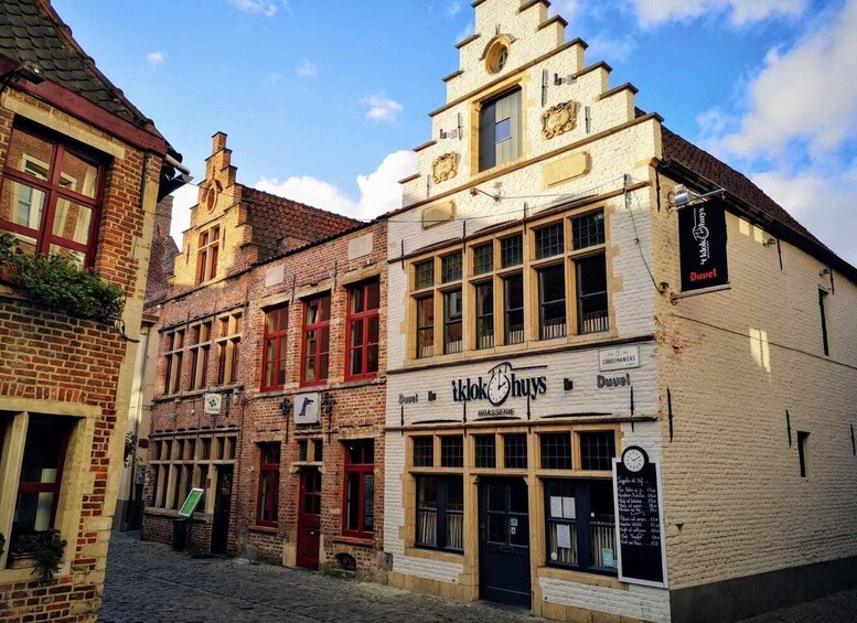 A cobblestone street with historic buildings, including a white building with a sign for 'tklok Chuy's Brasserie'. 1