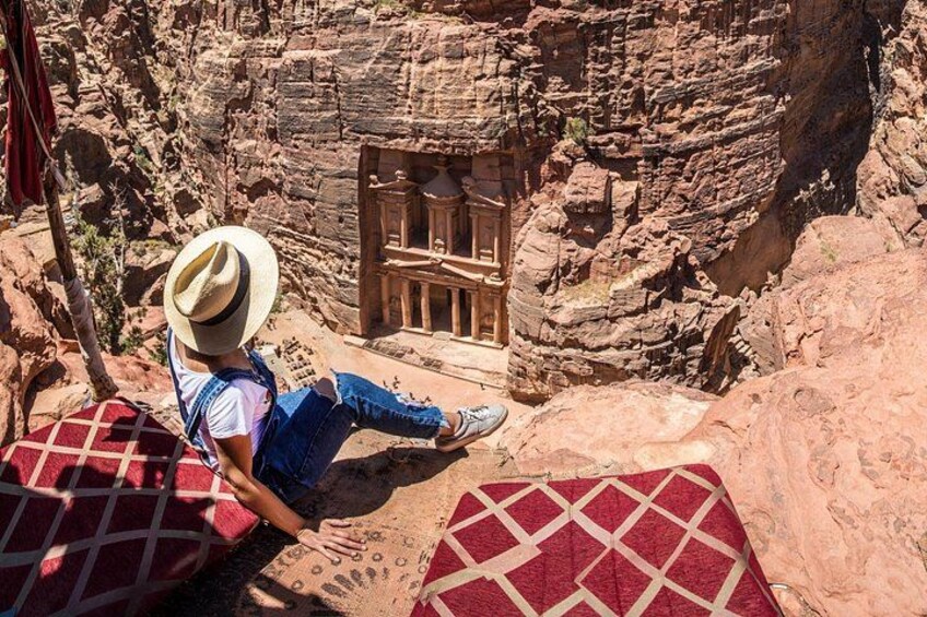 Une personne est assise sur une couverture rouge et blanche à motifs, dans un canyon rocheux, avec une structure en bois en arrière-plan. 5