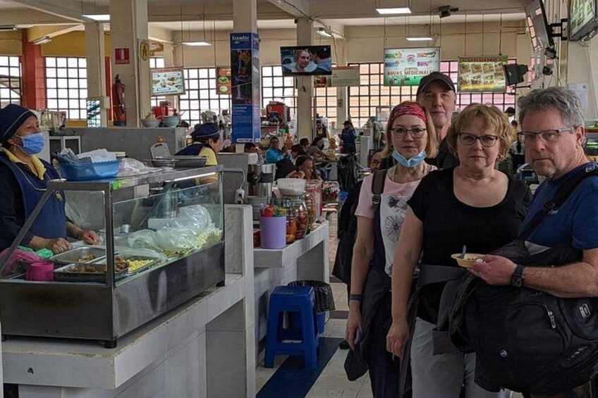 Un área de comidas concurrida, gente de pie comiendo, un mostrador con alimentos y un taburete azul. 4