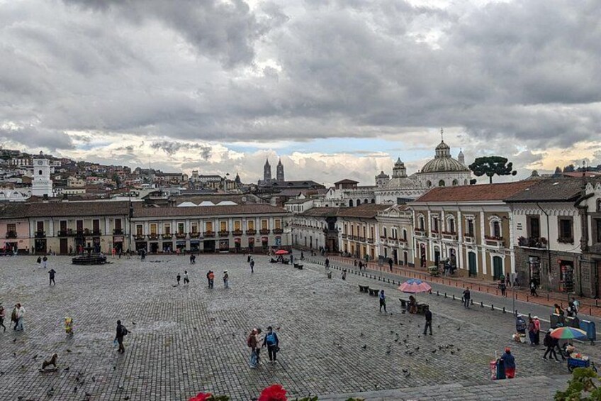 Una plaza adoquinada con edificios históricos, una fuente y una estructura con cúpula al fondo. 3