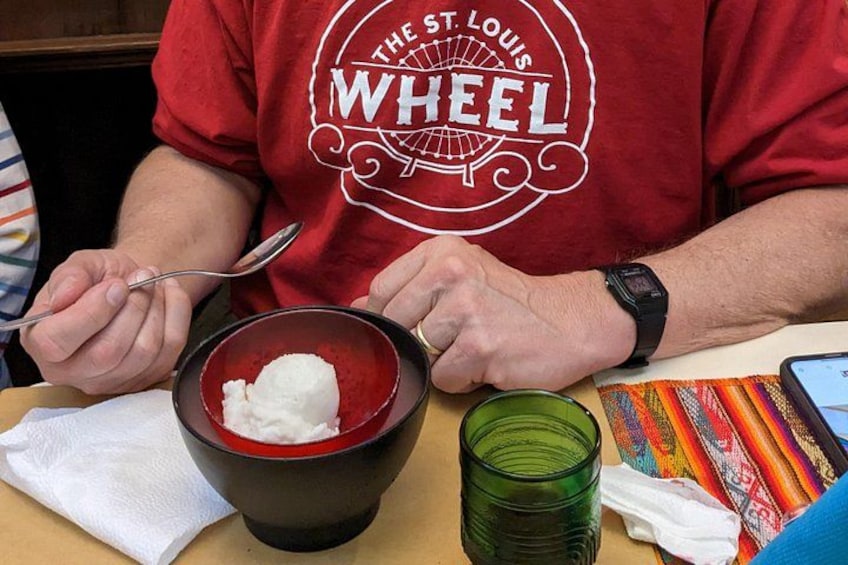 Una persona con una camiseta roja con un logo, comiendo helado de un tazón negro. 2