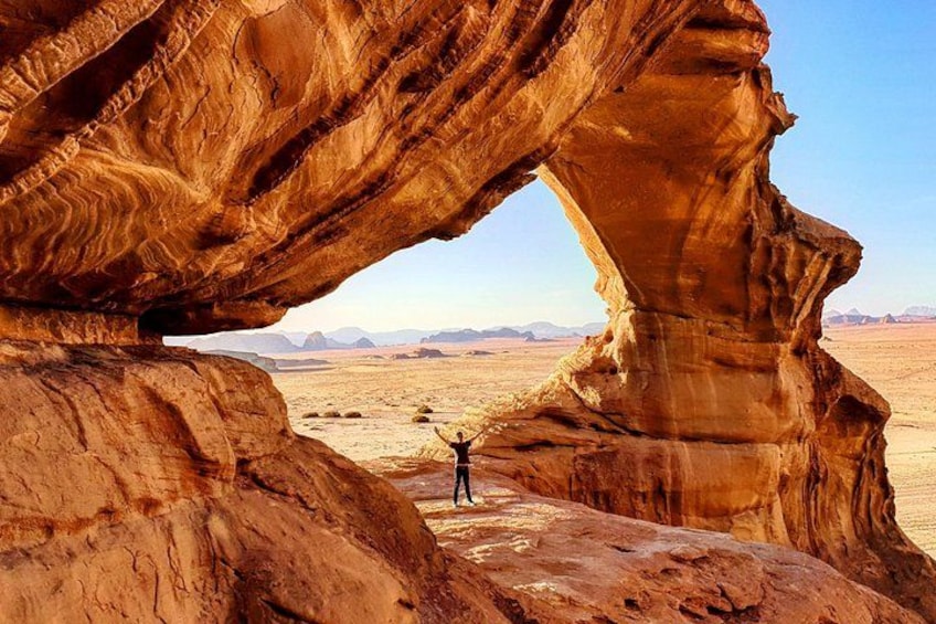 Une personne se tient sous une arche naturelle formée par la roche, dans un paysage désertique. 5
