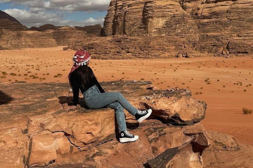 Una persona sentada sobre una roca en un paisaje desértico con formaciones rocosas rojas al fondo. 3