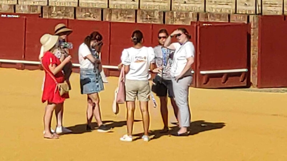 A group of people standing on a sandy surface with a red wall in the background. 1