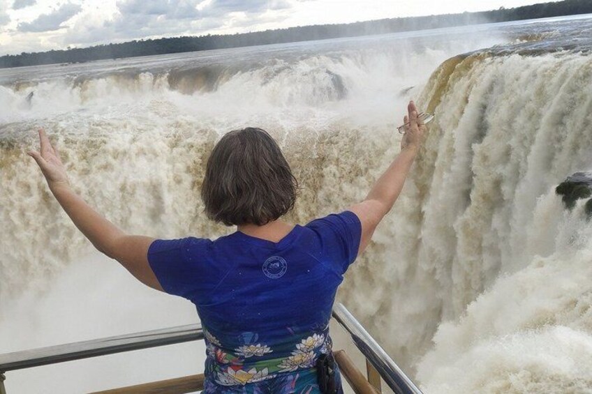 A person standing on a railing, facing a large waterfall. 2