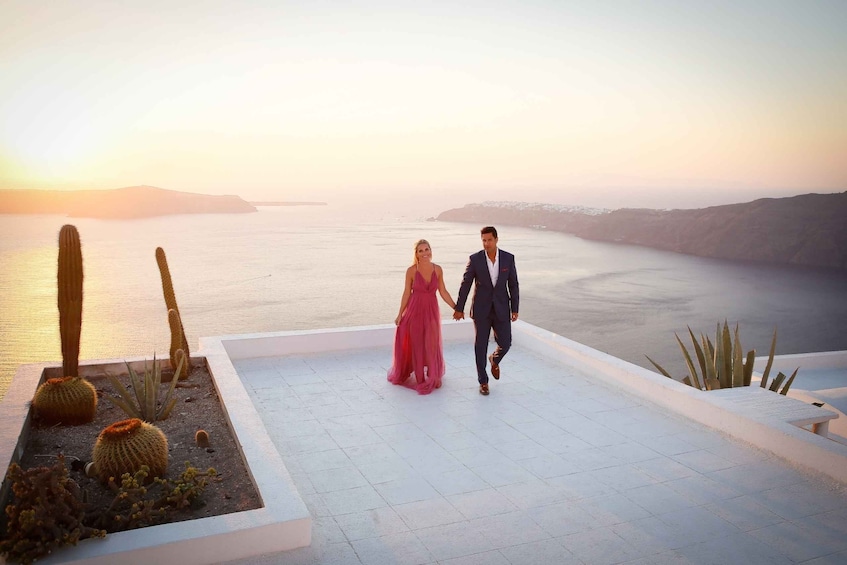 Una pareja caminando en una terraza en la azotea con vistas a un cuerpo de agua al atardecer. 1