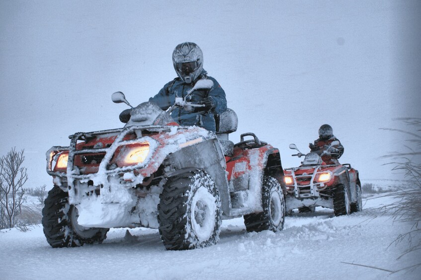 Two snow-covered ATVs with riders in winter gear. 2