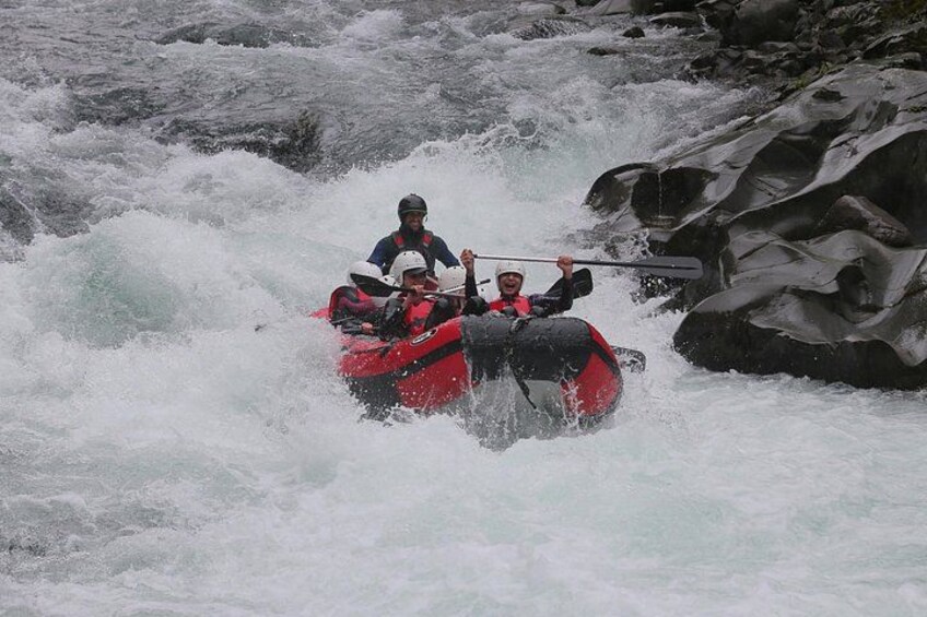 A group of people in a red raft navigating through a river with rapids. 4