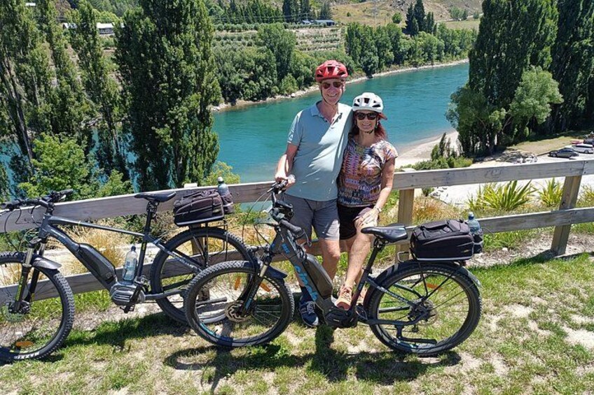 Twee personen staan naast fietsen op een grasveld met uitzicht op een meer en bomen. 5