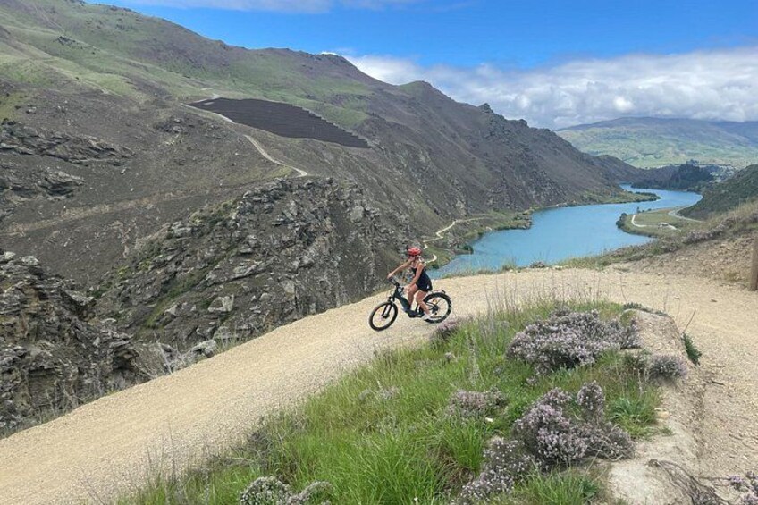 Een mountainbiker op een onverhard pad, met een meer en bergen op de achtergrond. 1