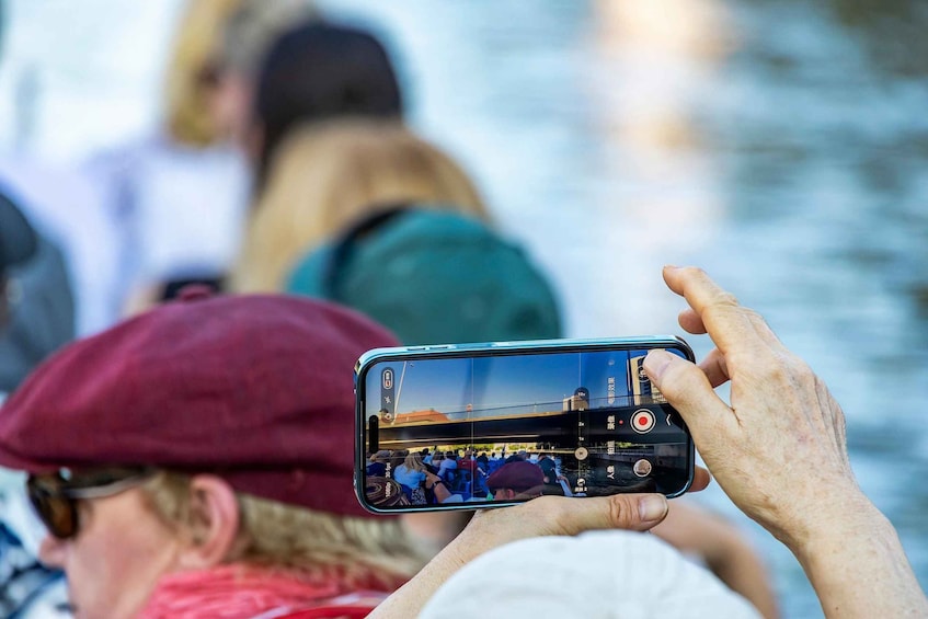 Una persona sosteniendo un teléfono inteligente, fotografiando un puente con gente. 4