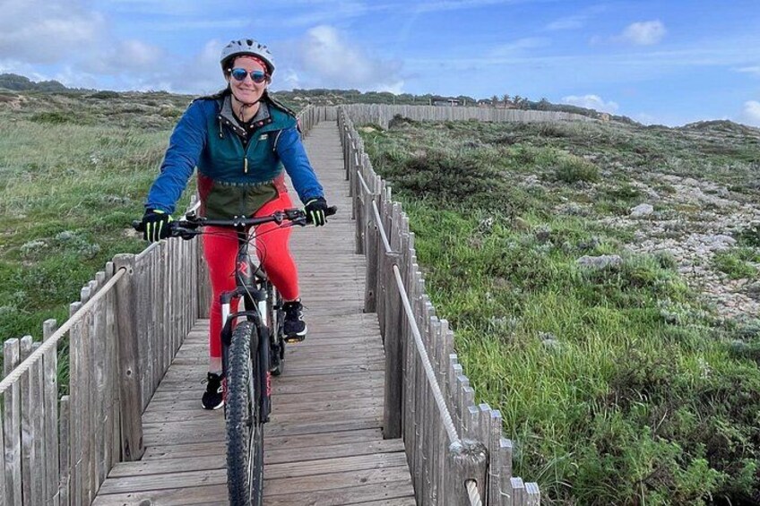 A person riding a bicycle on a wooden boardwalk through a grassy landscape. 5