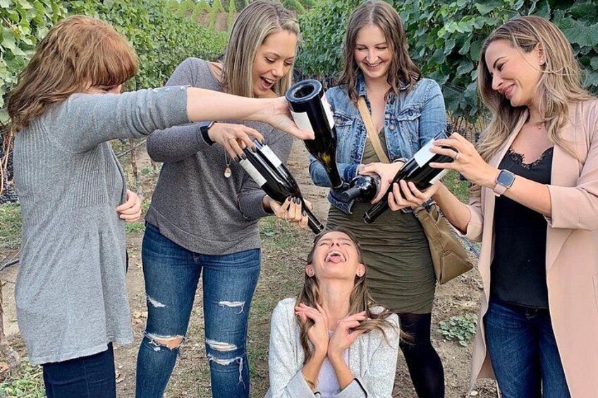 A group of people holding wine bottles, standing in a vineyard. 5