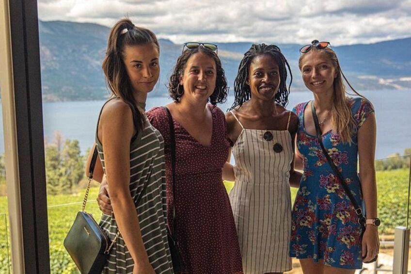 Four people standing by a window overlooking a lake and mountains. 5