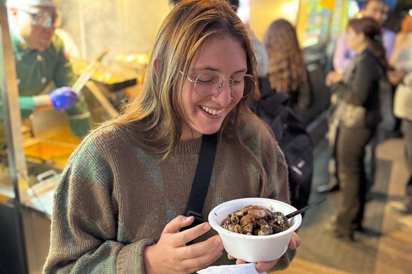 A person holding a bowl of food, with other people in the background. 4