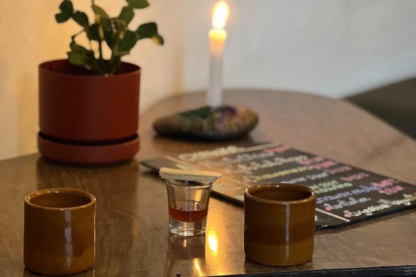 A wooden table with two mugs, a shot glass, a candle, and a potted plant. 1
