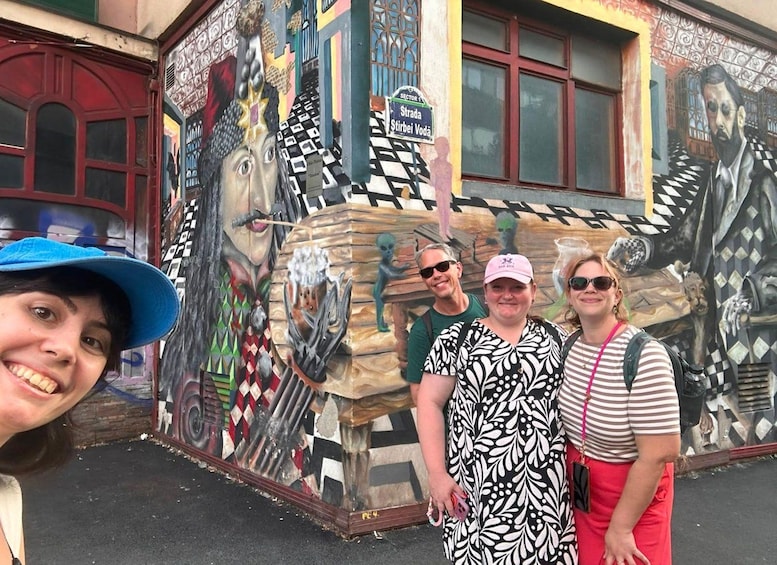 Un grupo de personas frente a un mural colorido con patrones geométricos y un edificio con puerta roja. 3