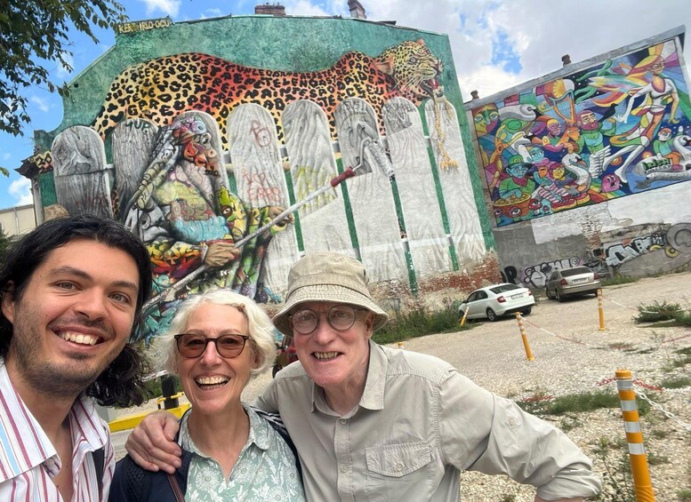 Un mural con un jaguar y figuras coloridas, una persona con sombrero, y un coche estacionado cerca. 2