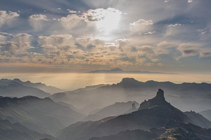 A mountain range with a prominent peak and a sun shining through the clouds. 4