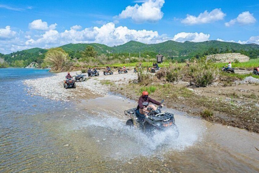 A riverbank with people on quad bikes, a clear sky, and green hills in the background. 5