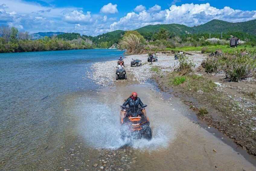 A person riding a quad bike through shallow water on a riverbank. 2