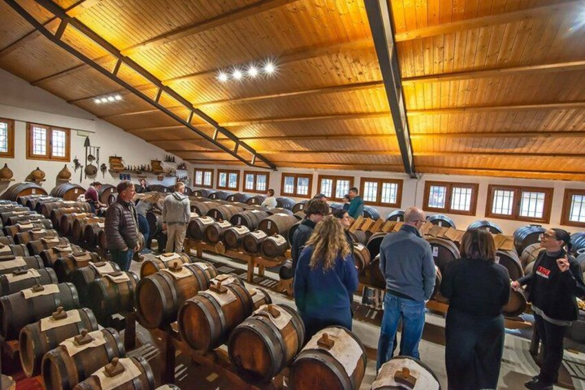 Una habitación amplia llena de barriles de madera, probablemente para vino u licores, con gente examinándolos. 3