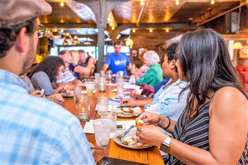 A group of people dining at a restaurant with wooden tables and hanging lights. 1