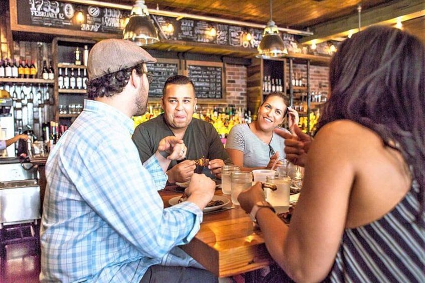 A bar with people sitting at tables, bottles on shelves, and a chalkboard menu. 4