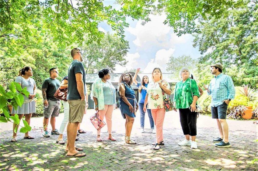 A group of people standing outdoors in a garden with trees and a paved walkway. 2