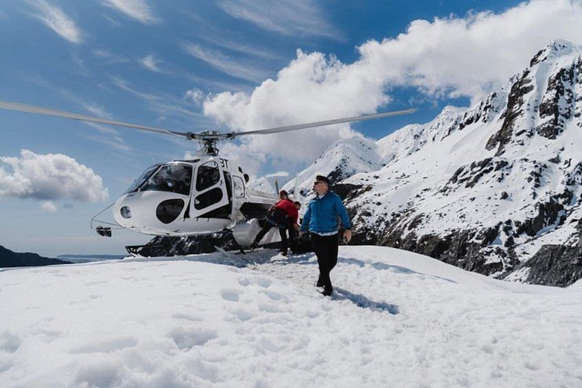 A helicopter on a snowy mountain with a person in a blue jacket walking nearby. 2