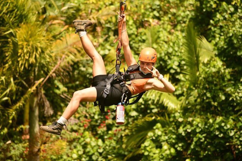En person som hoppar bungyjump med säkerhetssele och hjälm, omgiven av tät, grön vegetation. 2