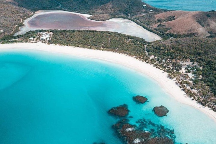 A coastal landscape with a sandy beach, clear turquoise waters, and rocky outcrops. 2