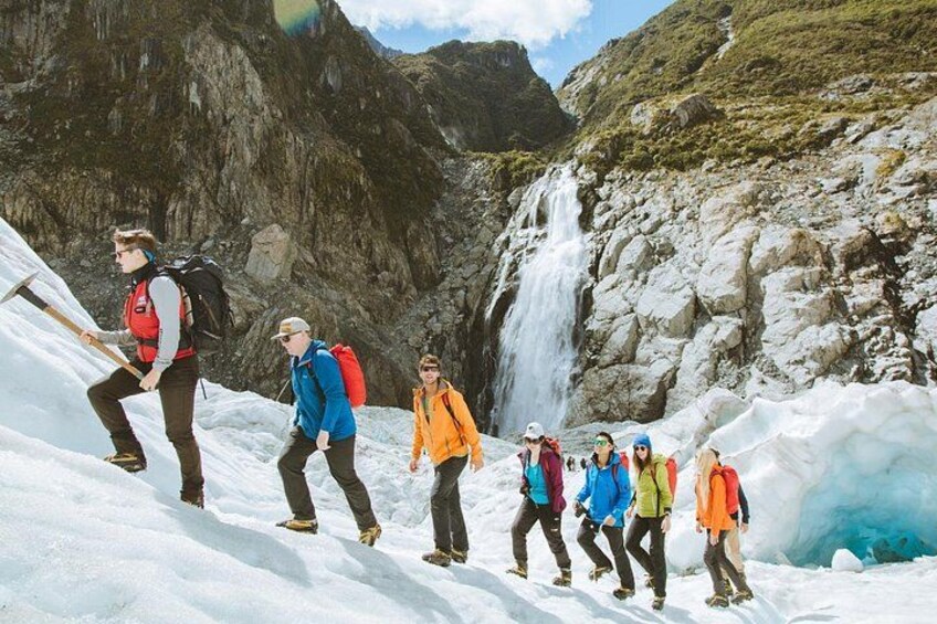 A group of hikers on a snowy mountain trail with a waterfall in the background. 5