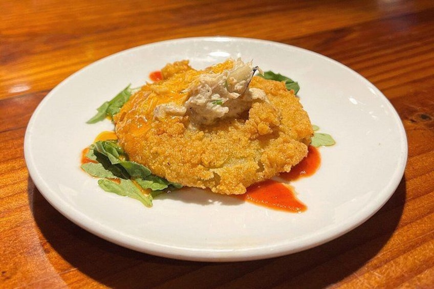 A white plate with a breaded food item, possibly chicken, garnished with greens and sauce. 4