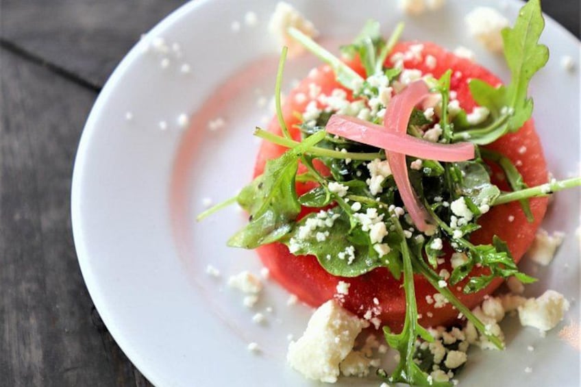 A white plate with a salad consisting of arugula, feta cheese, and red onion slices. 5