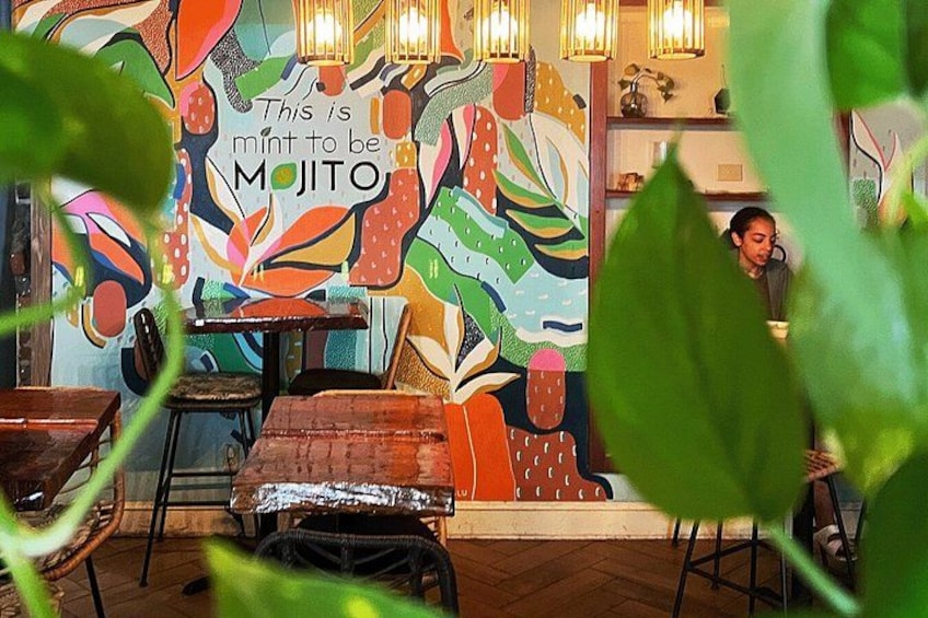 A restaurant interior with colorful murals, wooden tables, and a person in the background. 3