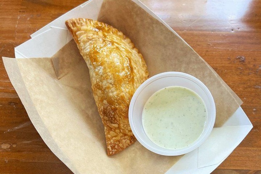 A pastry in a paper container with a dipping sauce. 2