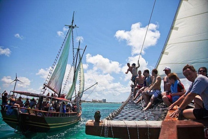 A traditional sailing boat with people on deck and a smaller boat nearby. 1