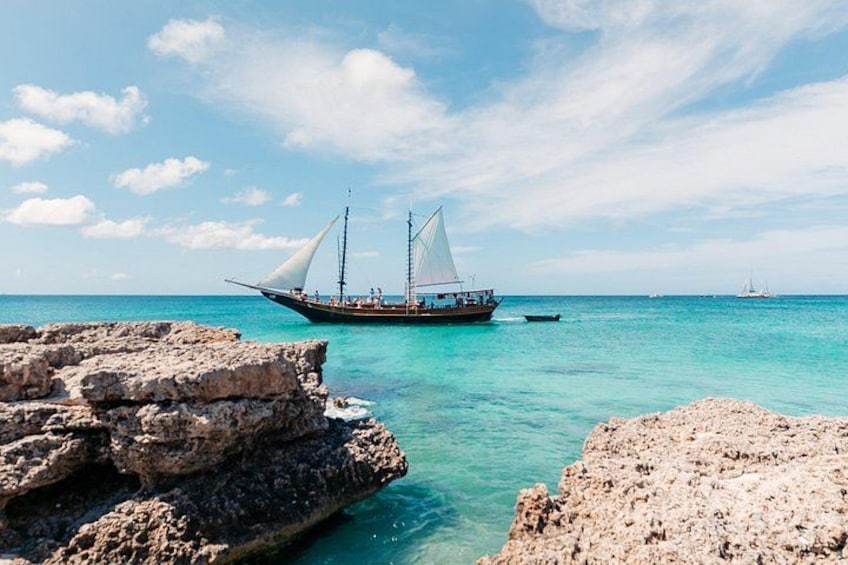 A sailboat with two masts sailing on turquoise waters near rocky shores. 3
