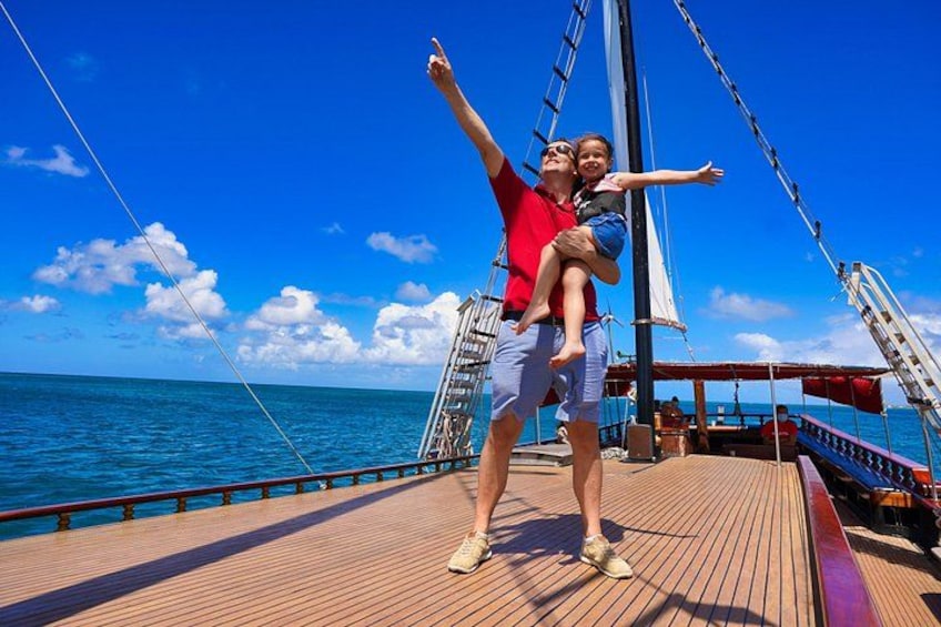 A person holding a child on a wooden deck of a sailboat with the ocean and sky in the background. 4