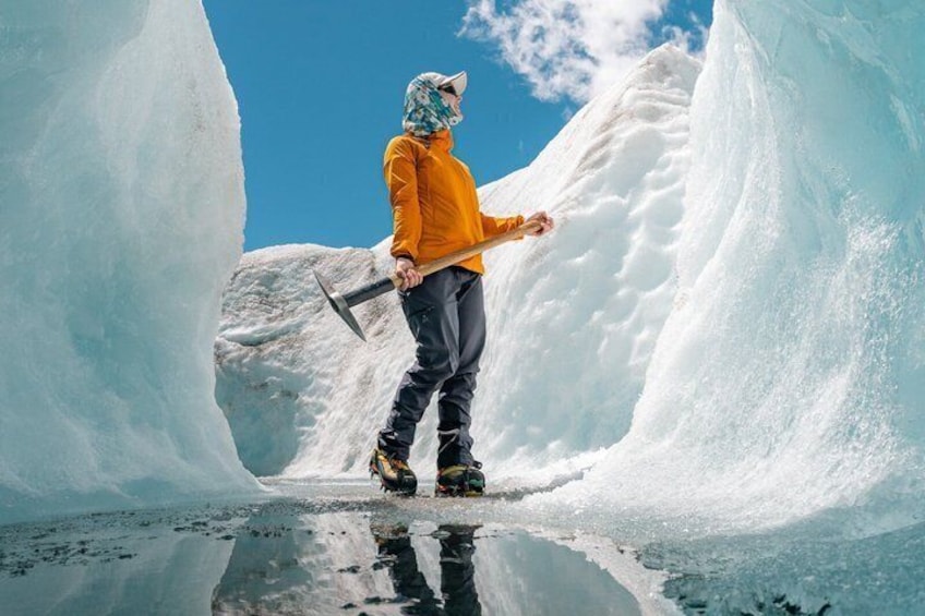 A person in a yellow jacket and helmet standing in a snow-covered ice cave with an axe. 1