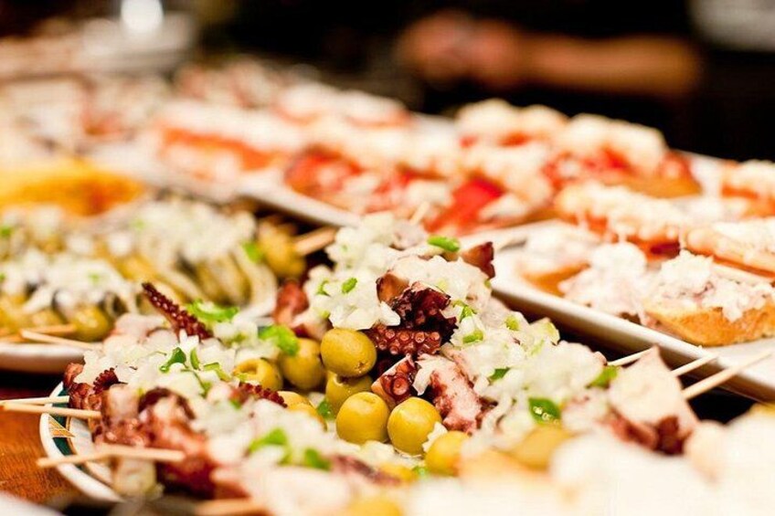 A variety of tapas dishes on skewers, including olives, cheese, and possibly seafood, arranged on a table. 2