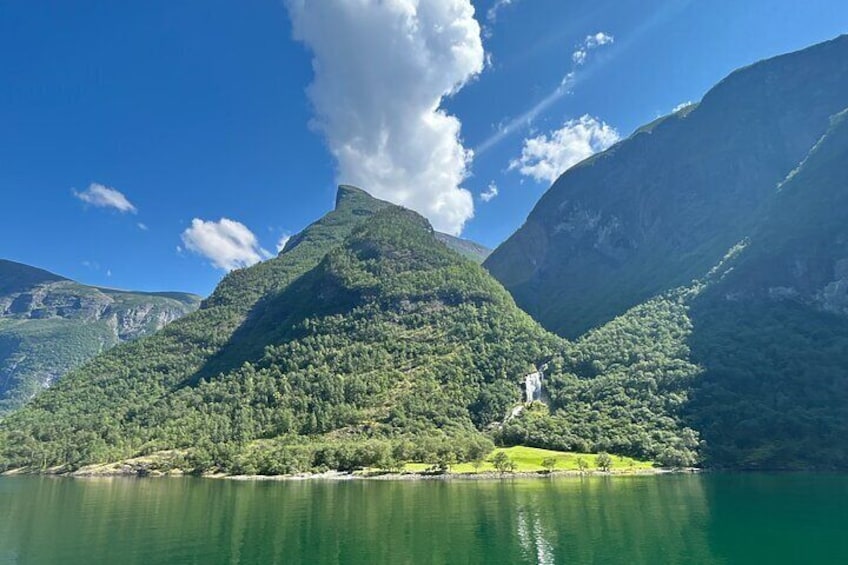 A mountain lake with a waterfall, surrounded by lush greenery and clear blue skies. 3
