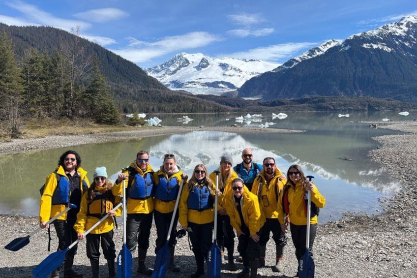 Un groupe de personnes vêtues de vestes jaunes se tient près d’un lac, avec des montagnes en arrière-plan. 3