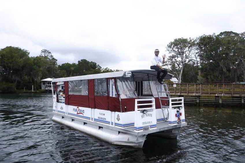 Una casa flotante con una persona de pie en la cubierta, rodeada de agua y árboles. 2